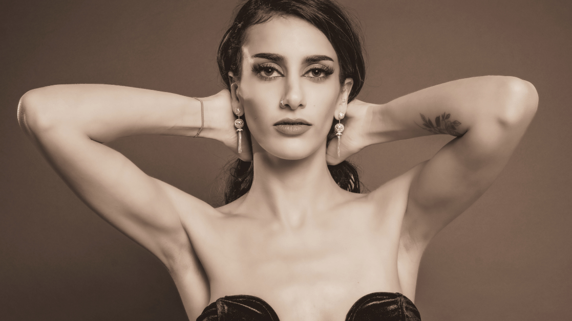 Black and white portrait of a woman with her hands behind her head against a brown background